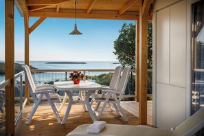 Eine Holzterrasse mit Tisch und Stühlen, mit Blick auf ein Gewässer und entferntes Land.
