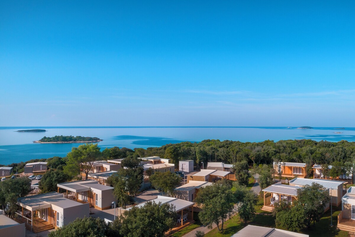 Eine Küstenlandschaft mit mehreren Mobilheimen, blauem Himmel und Blick auf das Meer und Inseln in der Ferne.