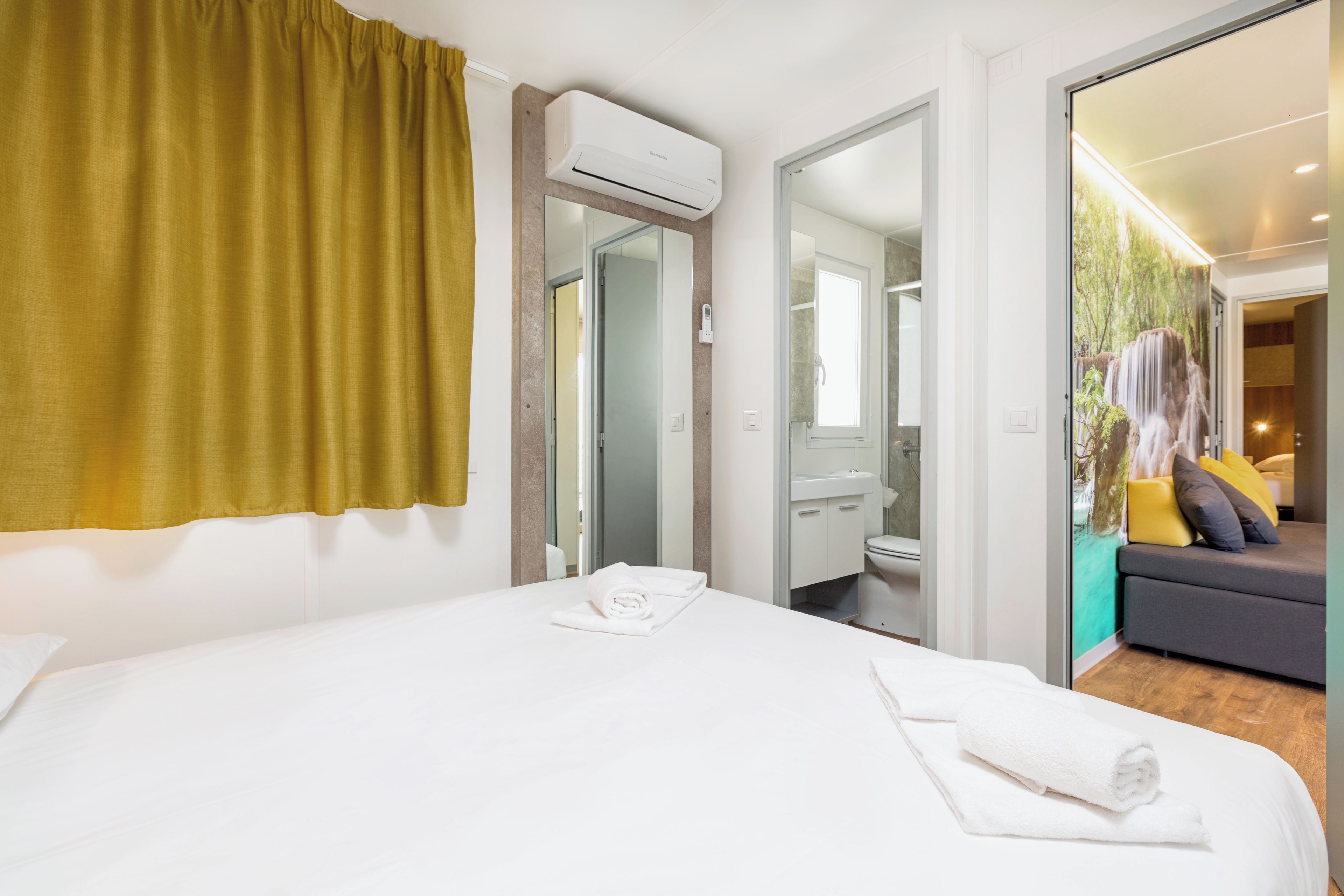 Una habitación de hotel con cama, baño y sala de estar con sofá y cojines.