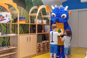 Een kamer met houten kasten, een plank met kleurrijke spullen en een groot blauw wezen als mascotte.