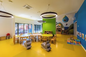 Une salle de classe bien éclairée, avec un sol jaune, des tables et des chaises en bois, et un mur d’accent vert.