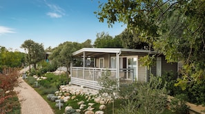 Ein eingeschossiges Haus mit einer überdachten Veranda, umgeben von einem Garten mit verschiedenen Pflanzen und einem Weg.