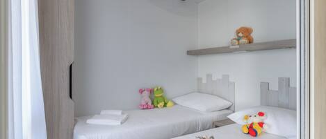 Une chambre avec deux lits, une armoire et une étagère où sont posés des animaux en peluche.