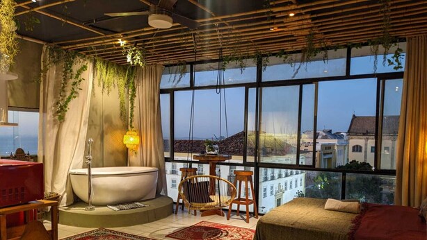 Un baño moderno con bañera, ducha y ventana con vistas a un paisaje urbano.