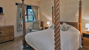 A four-poster bed with a wooden frame, a wooden dresser, a chair, and a nightstand with a lamp. - Billy's Barn (Holsworthy)