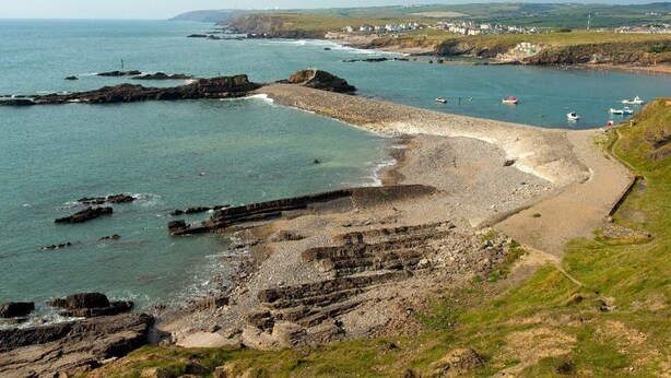 A coastal landscape with rocky terrain, a sandy beach, and boats in the water. - Billy's Barn (Holsworthy)
