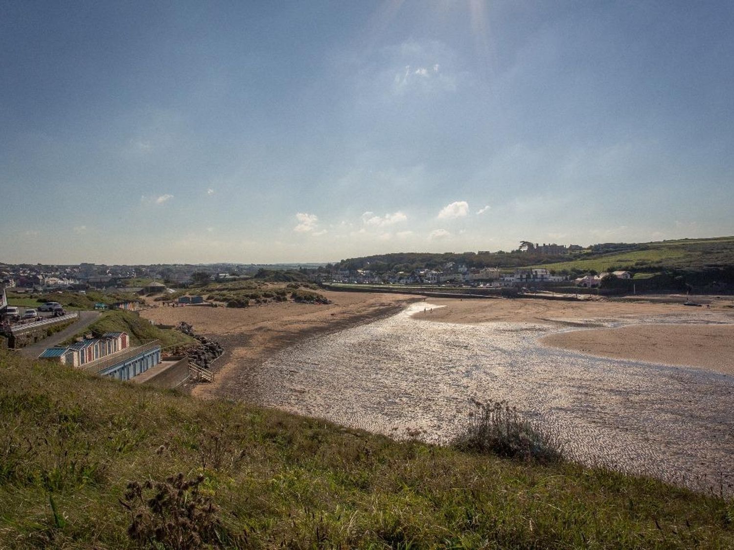 Un paisaje costero con una playa, un edificio pequeño con techo azul y un pueblo lejano.