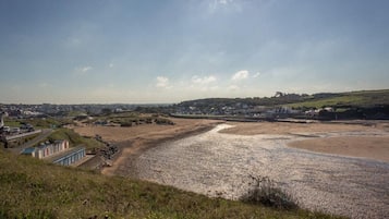 Un paisaje costero con una playa, un edificio pequeño con techo azul y un pueblo lejano.