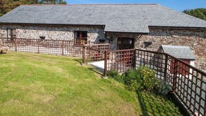 A stone building with a sloped roof, a fenced courtyard, and a grassy lawn. - Billy's Barn (Holsworthy)