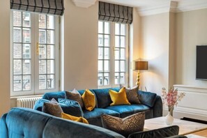 Ein Wohnzimmer mit blauem Sofa, gemusterten Kissen, einer Vase mit Blumen und einer Lampe.