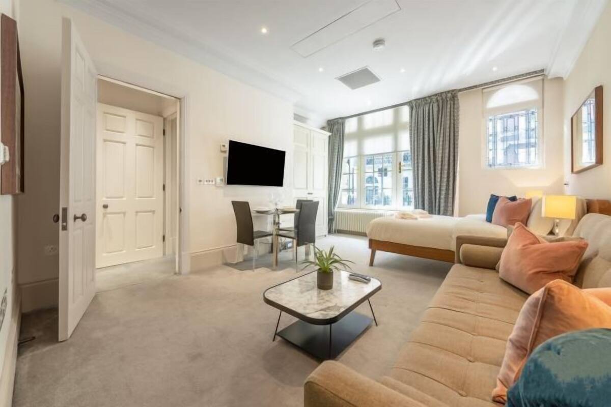 Une chambre d’hôtel moderne équipée d’un canapé, d’une télévision, d’un bureau avec une chaise et d’une fenêtre avec des rideaux.