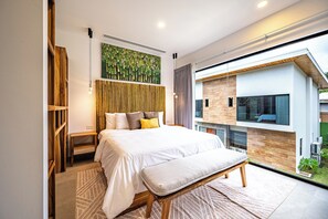 A modern bedroom with a large bed, a bench, a wooden headboard, a wall-mounted artwork, and a view of the outside. - Double the space, double the fun ! 2 Brand New Luxury Villas, Gated Community (Jaco)