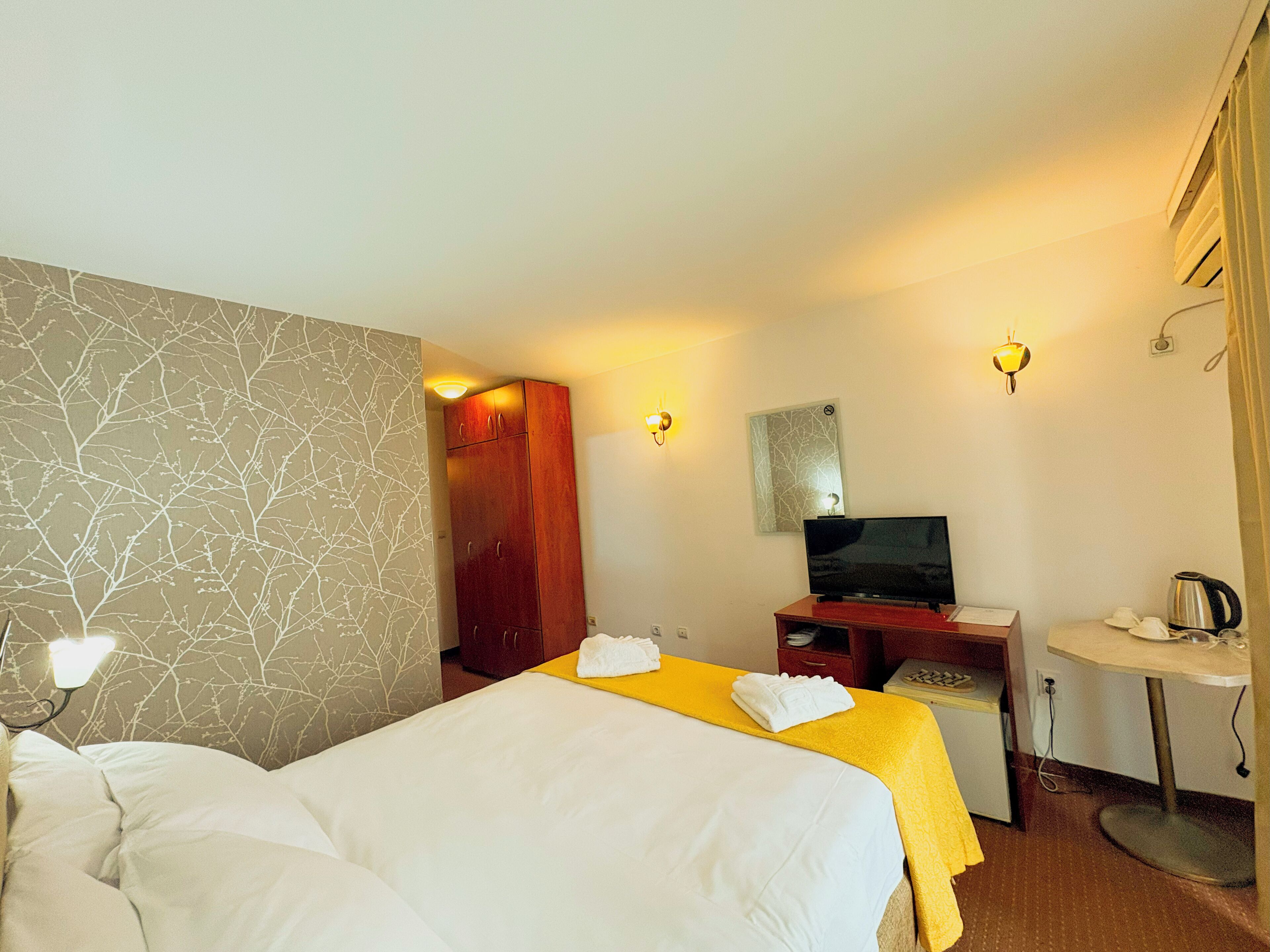 A hotel room with two beds, a TV, a desk, and a small table with a kettle.