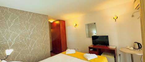 A hotel room with two beds, a TV, a desk, and a small table with a kettle.