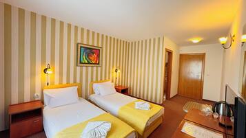 Een hotelkamer met twee bedden, een bureau met een computer, een televisie en een schilderij aan de muur.