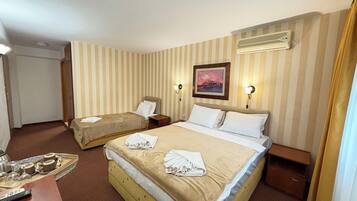 A hotel room with two single beds, a wooden headboard, a bedside table with a lamp, and a painting on the wall.