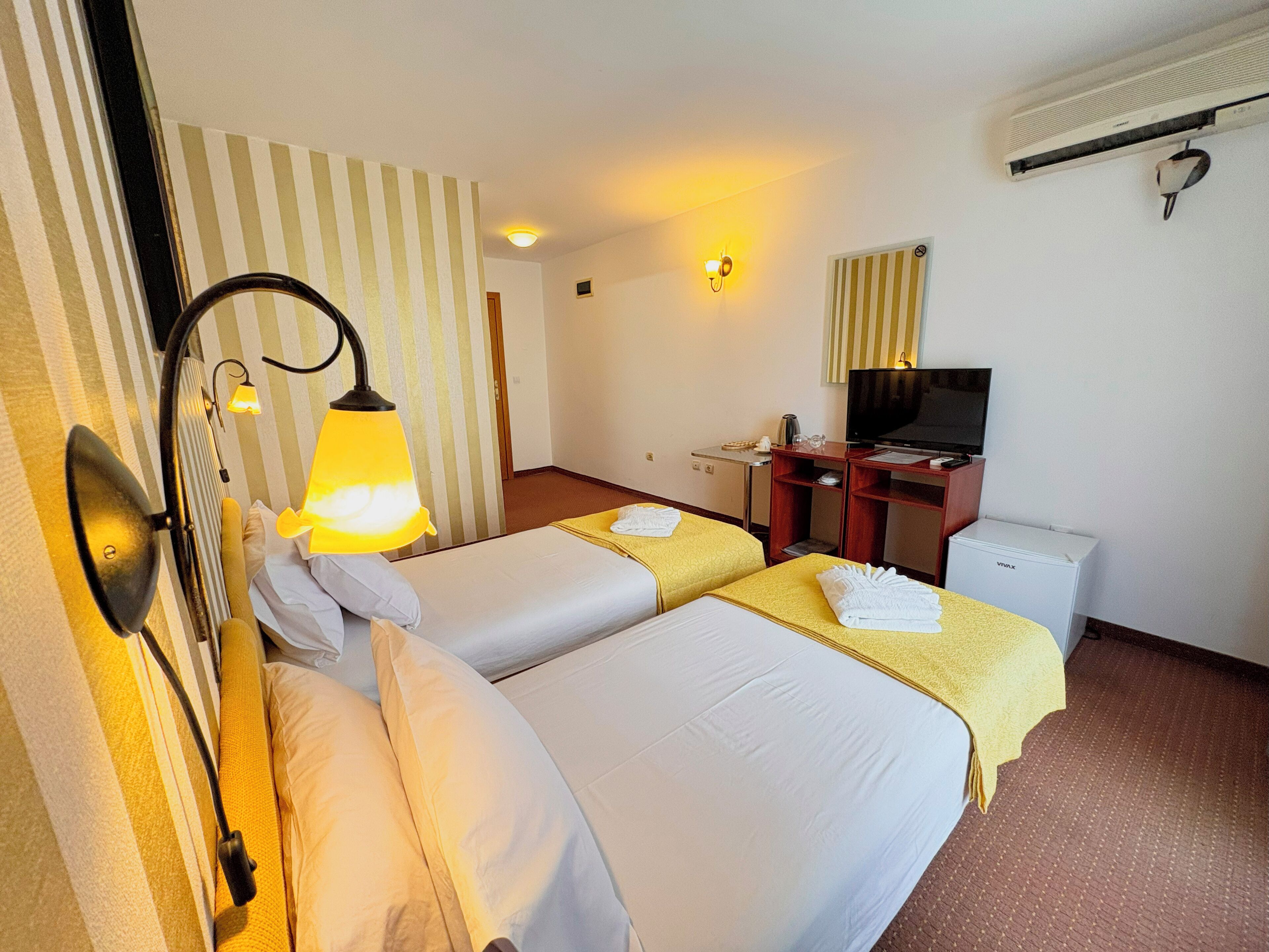 Une chambre d’hôtel avec deux lits, un bureau avec une télévision, un mini-bar et un climatiseur fixé au mur.