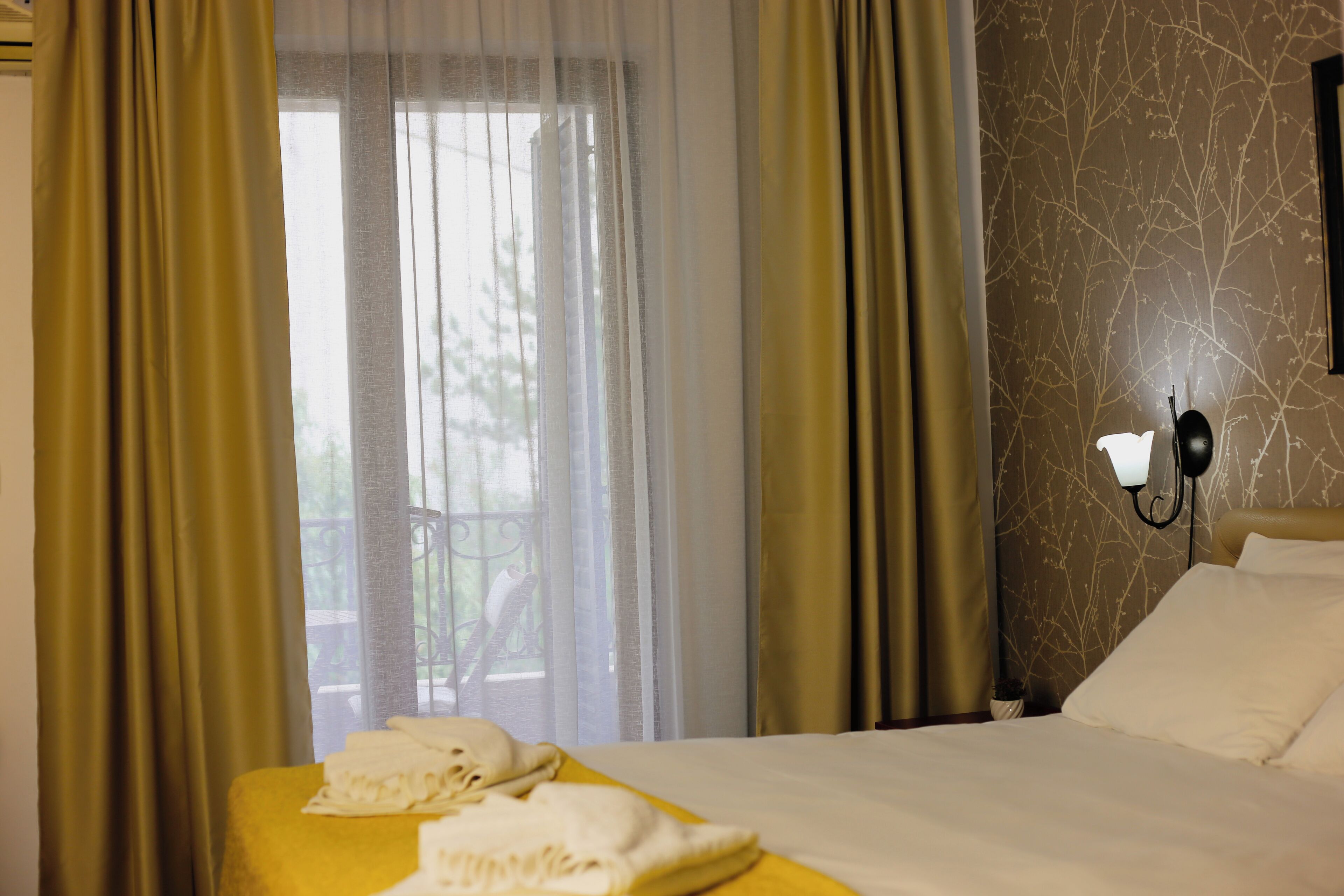 A hotel room with a bed, a telephone, and a window with curtains.