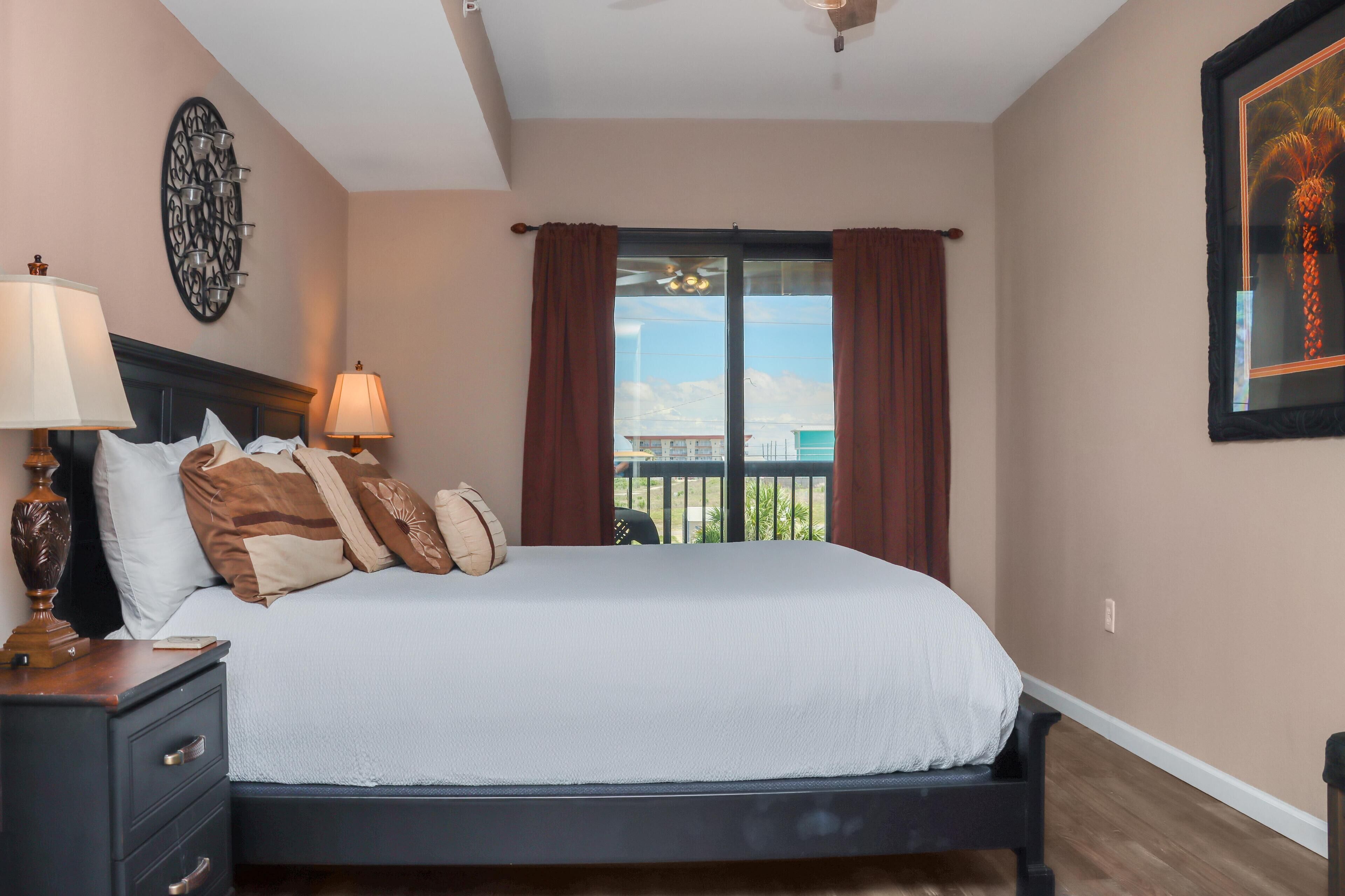 A bedroom with a bed, nightstands, a wall-mounted lamp, a ceiling fan, and a window with curtains.