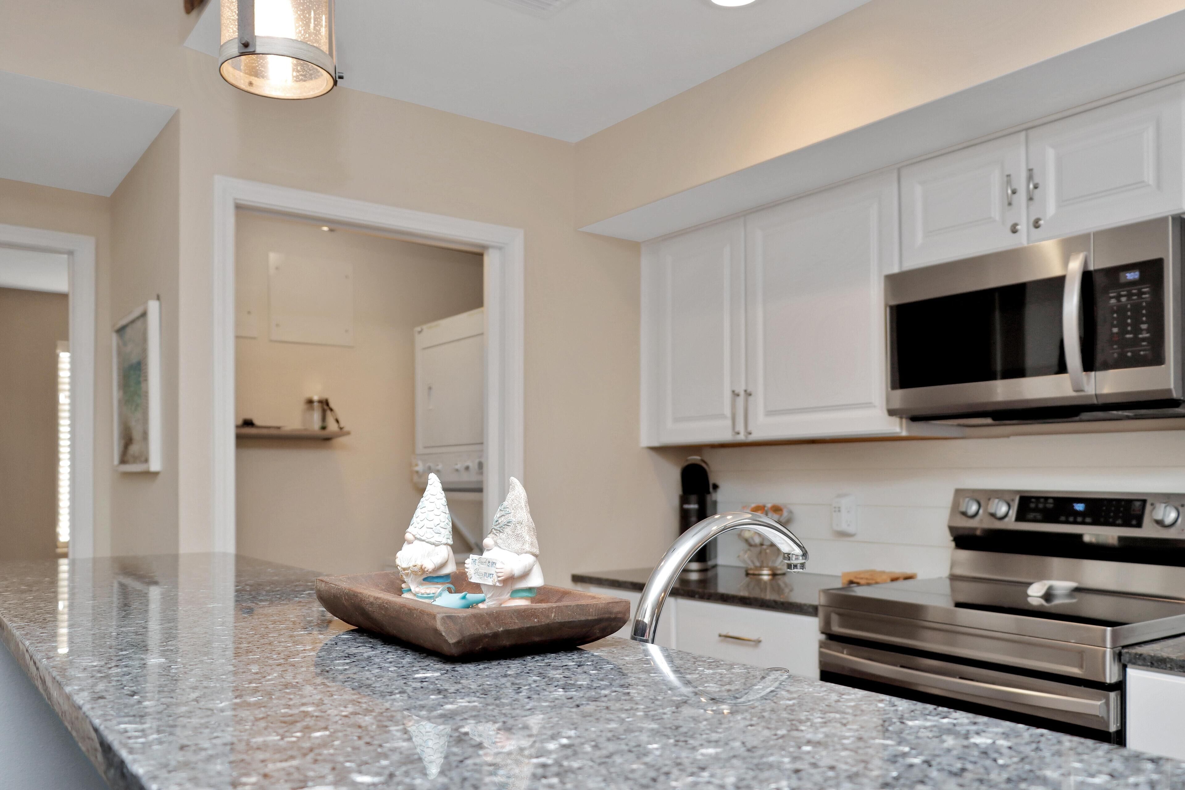 A modern kitchen with white cabinets, a stainless steel microwave, an oven, and a granite countertop.