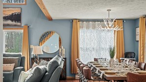 A dining area with a long table set for a meal, a sofa, and a large mirror. - Luxury 3-Story Pocono Retreat w/ Sauna+Hot Tub+Games (Albrightsville)