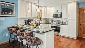 A modern kitchen with white cabinets, a central island with bar stools, a microwave, oven, and various kitchen appliances. - Luxury 3-Story Pocono Retreat w/ Sauna+Hot Tub+Games (Albrightsville)