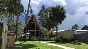 A triangular wooden structure with a window, surrounded by lush greenery and a clear sky.