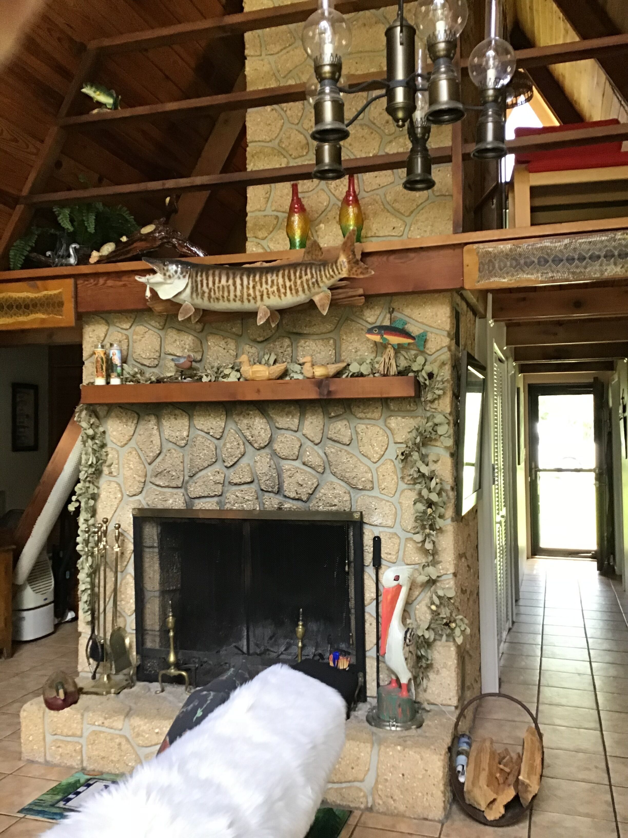 Ein rustikales Interieur mit Kamin aus Stein, Holzbalken und einer hängenden Leuchte.