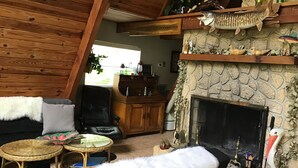 A cozy living room with a stone fireplace, wooden ceiling, and a comfortable seating area with a fur throw.