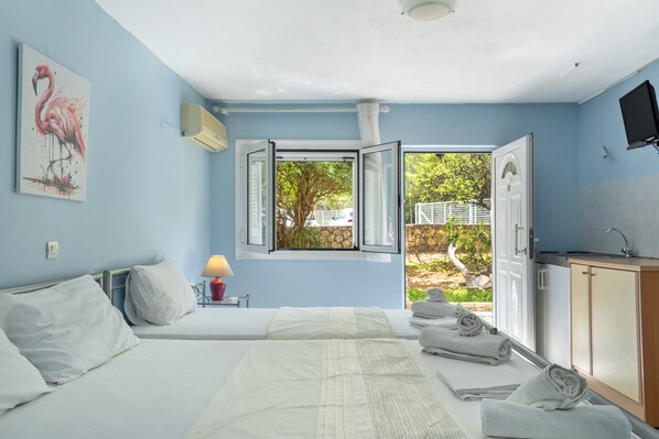 A bedroom with two beds, a window with an open view, a painting, and a TV.