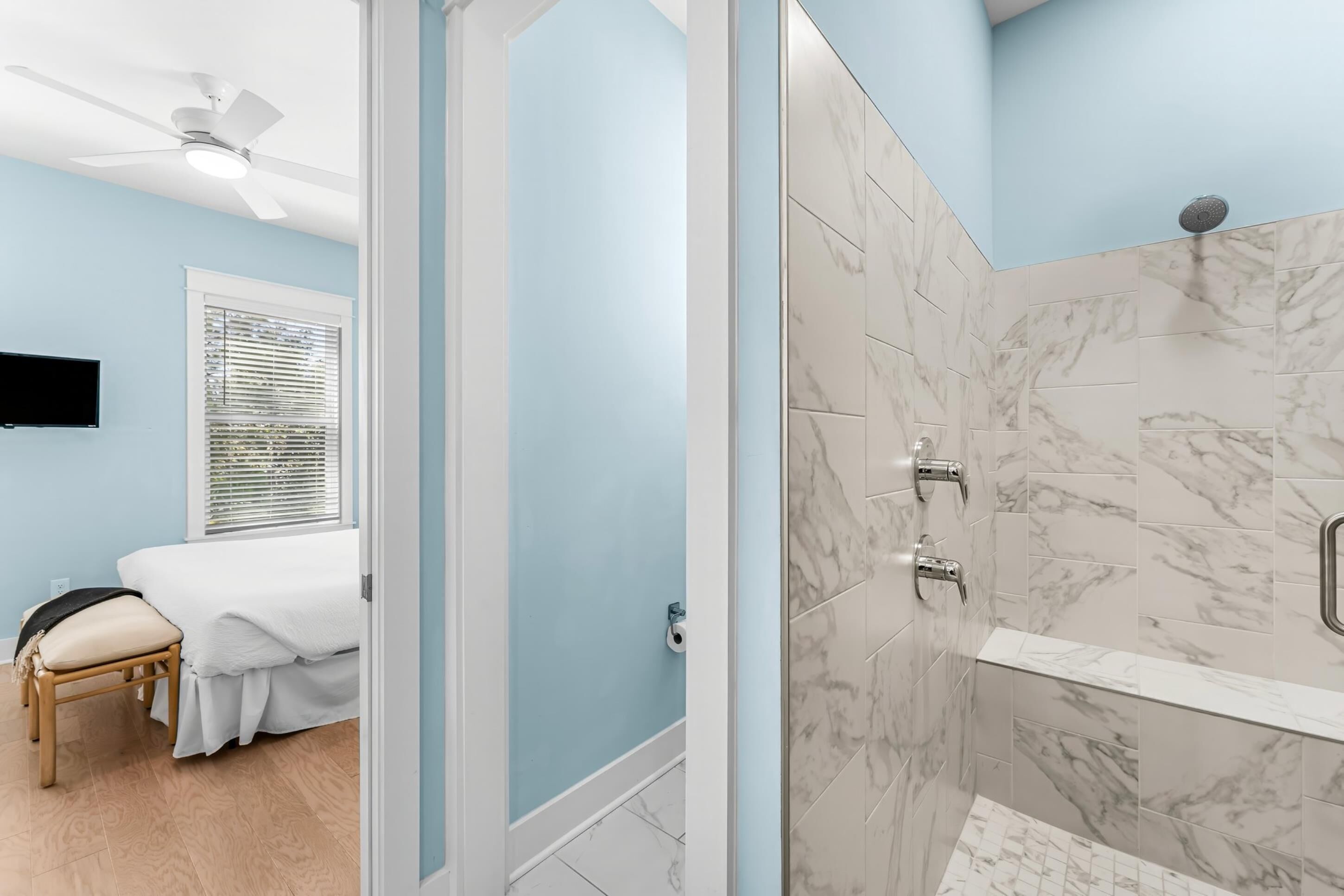 A bathroom with a shower, marble tiles, and a ceiling fan.