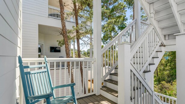 A wooden deck with a blue chair, white railings, and a staircase leading to an upper level. - 30A Beach House - Paradise Valle (Panama City Beach)