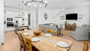A modern kitchen with white cabinets, a wooden dining table set with plates and glasses, and a chandelier. - 30A Beach House - Paradise Valle (Panama City Beach)
