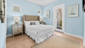 A bedroom with a large bed, a ceiling fan, a nightstand with a lamp, and a door leading to a balcony. - 30A Beach House - Paradise Valle (Panama City Beach)