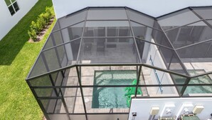 A glass-enclosed patio with a swimming pool and a green inflatable toy. - Family Friendly w Pool Near Disney at Serenity 1420 (Clermont)