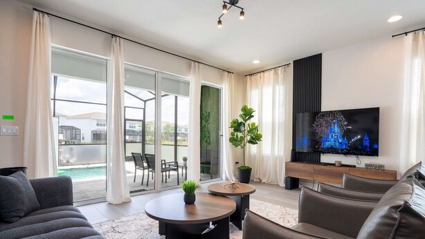 A modern living room with a flat-screen TV, two round coffee tables, a sofa, and a potted plant. - Family Friendly w Pool Near Disney at Serenity 1420 (Clermont)