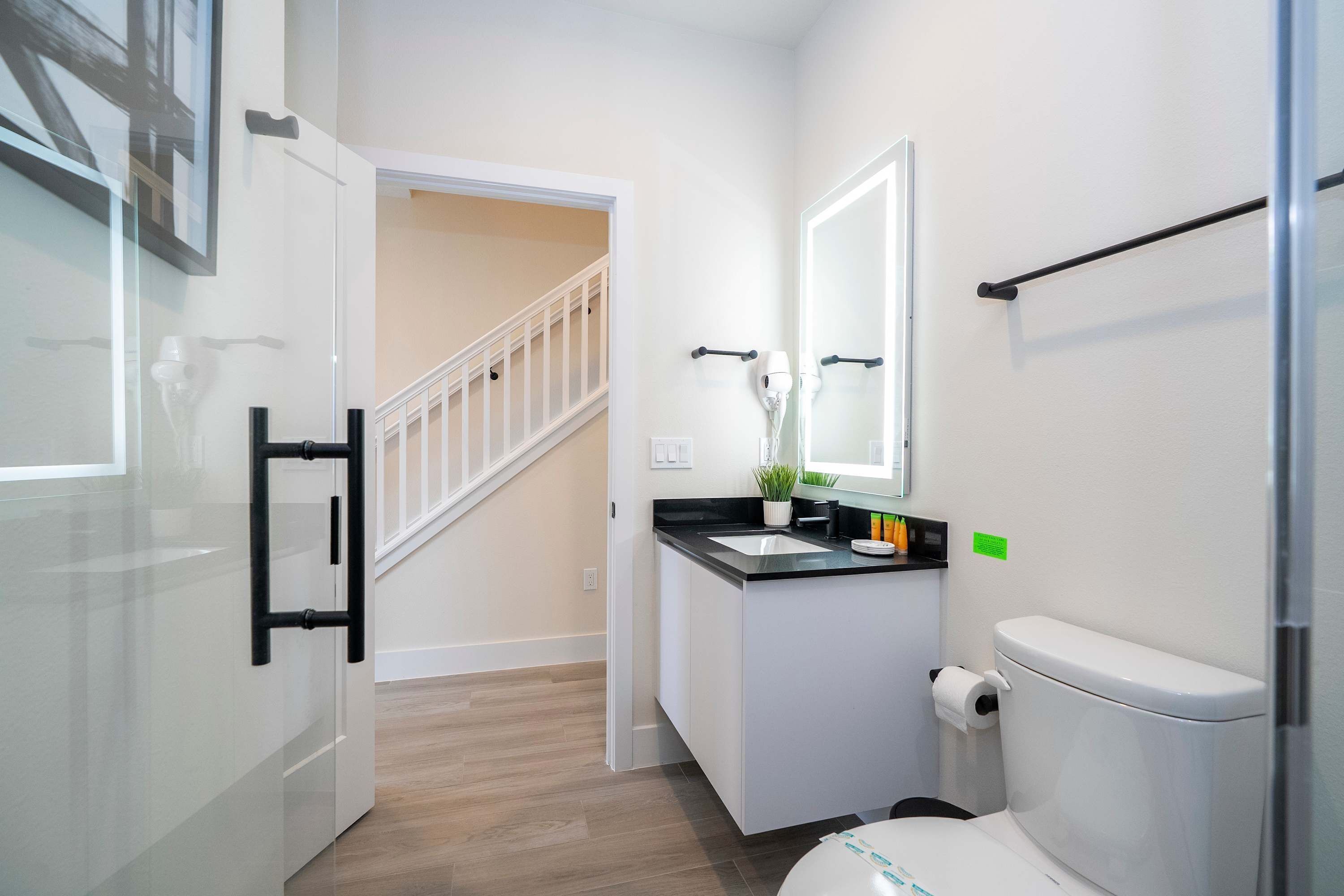 A modern bathroom with a white toilet, a sink with a black countertop, a mirror above the sink, and a staircase leading to another room.