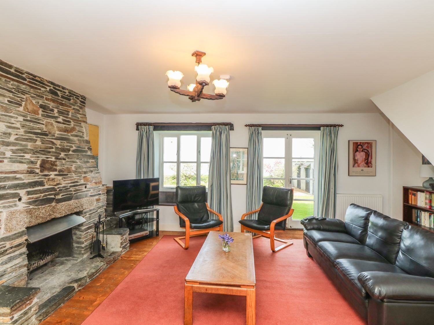 A living room with a stone fireplace, a television, two leather chairs, a wooden coffee table, and a black leather sofa.