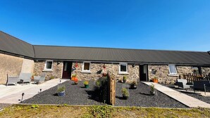 A stone building with a sloped roof, outdoor seating, and potted plants. - Bathach Mor (Oban)