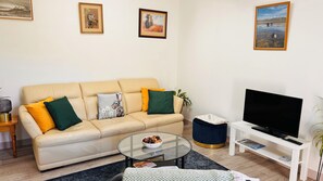 A living room with a beige sofa, a glass coffee table, a TV on a white stand, and framed pictures on the wall. - Bathach Mor (Oban)