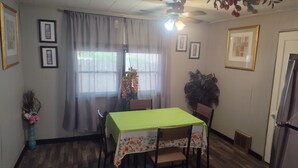 Uma sala de jantar com uma mesa posta para dois, um ventilador de teto e quadros nas paredes.
