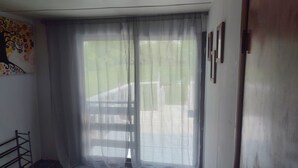 Quarto com uma janela grande coberta por uma cortina de tule xadrez, um suporte de metal e uma parede com uma pintura abstrata colorida.