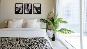 Ein modernes Hotelzimmer mit einem großen Bett, einer Zebradecke, drei abstrakten Wandbildern, einer Topfpflanze und Blick auf die Stadt durch das Fenster.