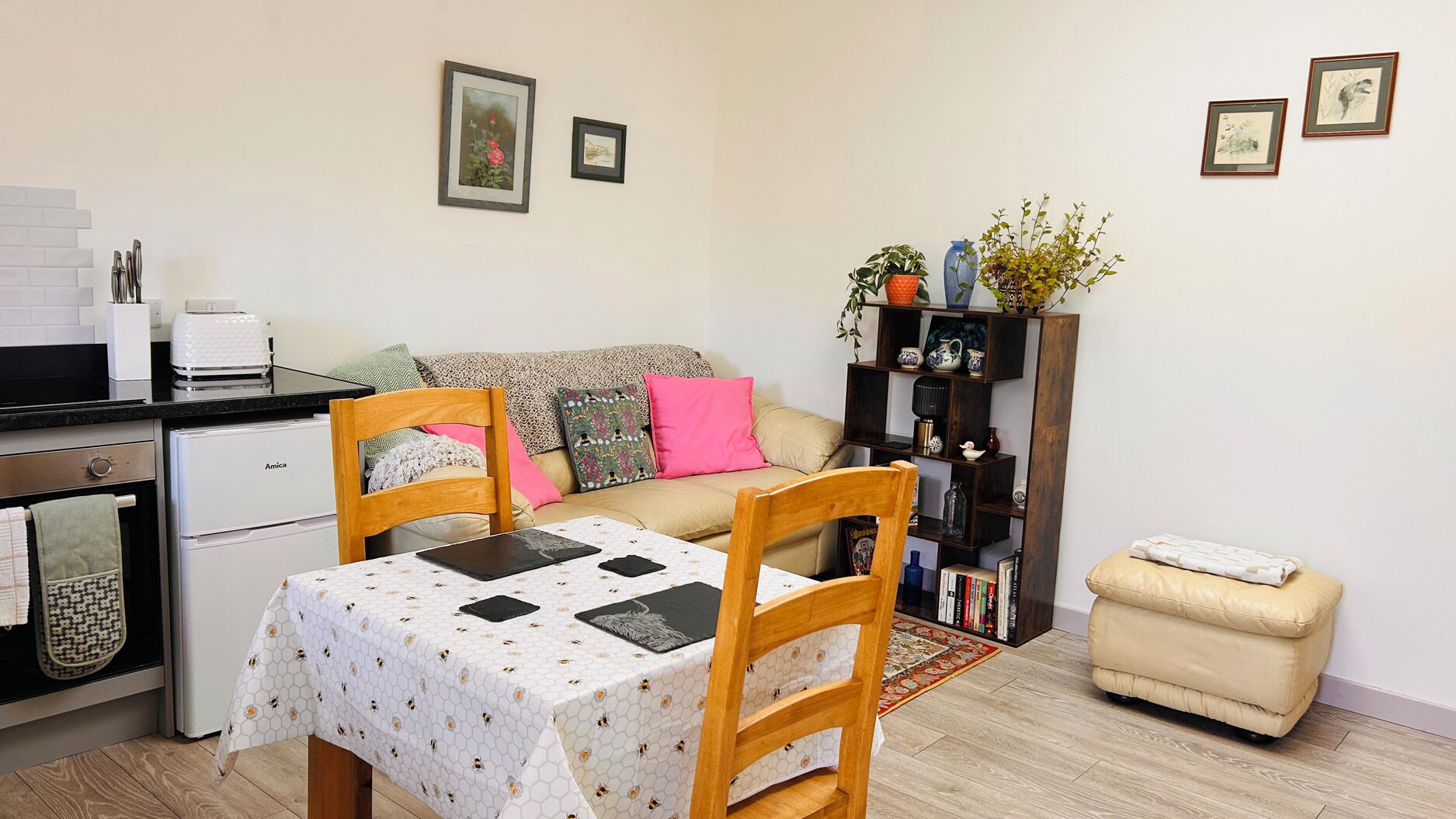A cozy living space with a dining table, chairs, a sofa, a small kitchenette, and a bookshelf.