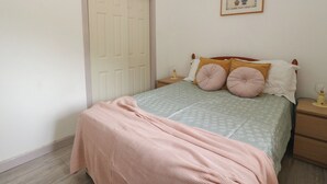 A bedroom with a bed, a nightstand, a bedside table, a door, and a framed picture on the wall. - Bathach Beag (Oban)