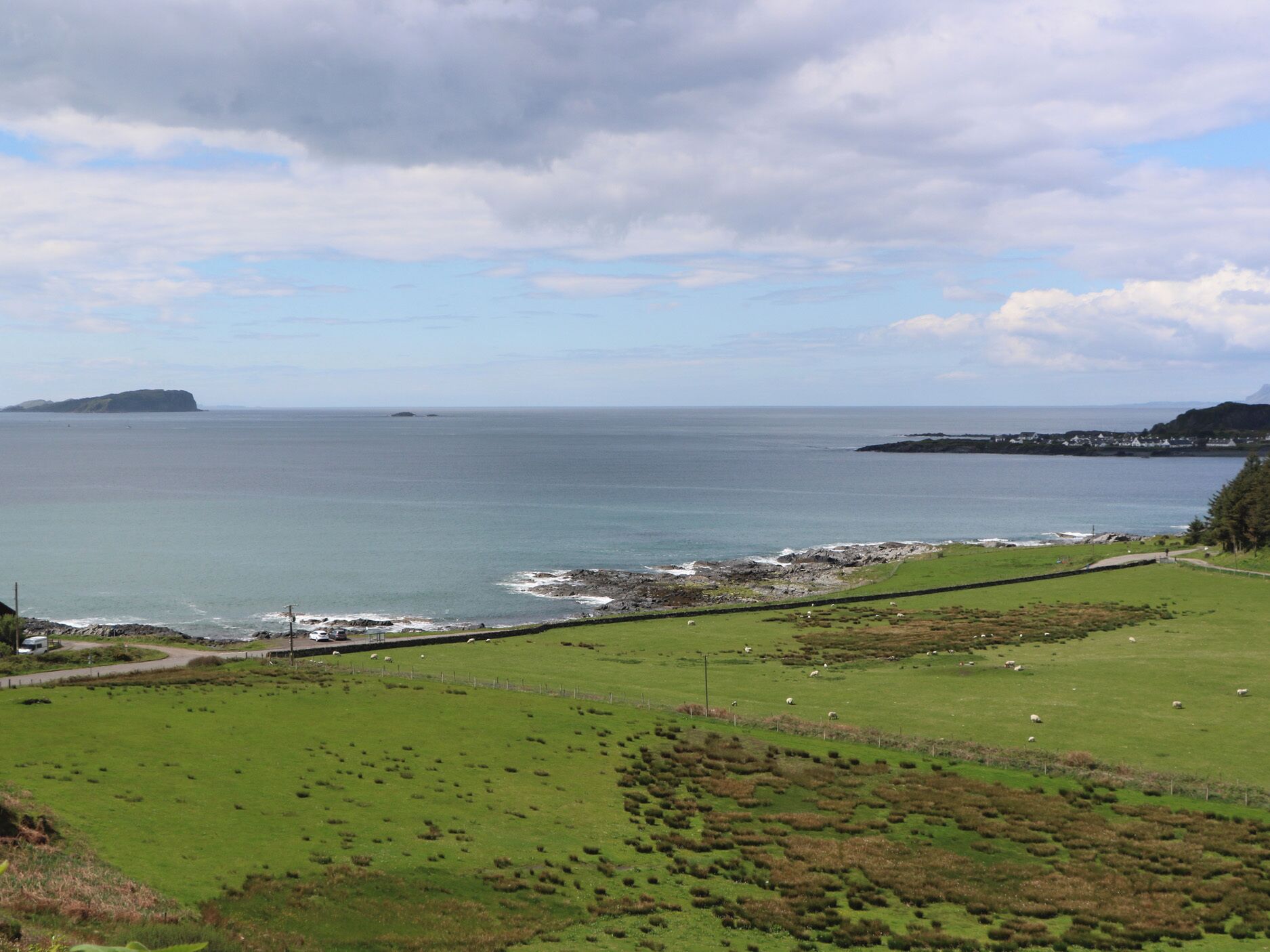 A coastal landscape with a grassy field, a rocky shoreline, and a distant island.