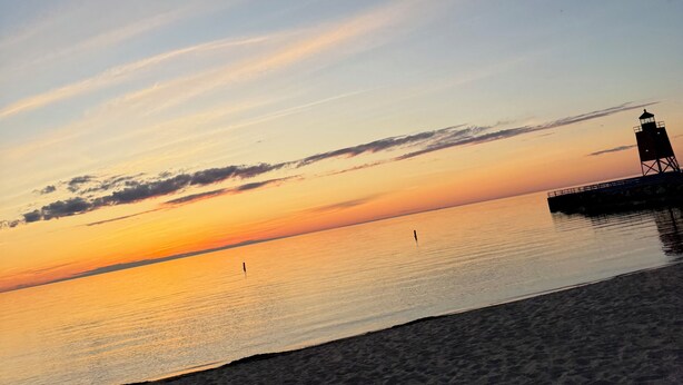 Una playa con un faro al atardecer.