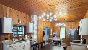 Una cocina con paneles de madera, una mesa de comedor central, armarios empotrados y una araña.