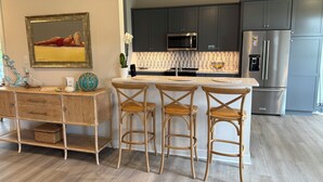 A modern kitchen with dark cabinets, stainless steel appliances, and a wooden bar area with three stools. - 3-bedroom house in charming Cape Charles with pool access. (Cape Charles)