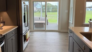 A modern kitchen with dark cabinets, stainless steel appliances, and a large sliding glass door leading to a balcony. - 3-bedroom house in charming Cape Charles with pool access. (Cape Charles)